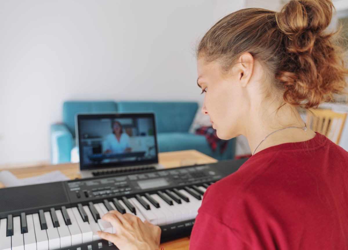 A woman with an laptop in front of her during a zoom call taking an online piano lesson
